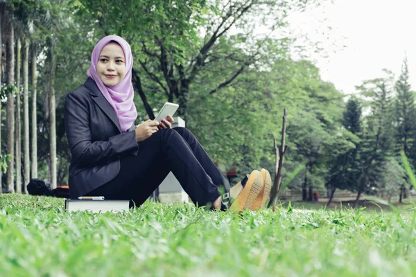 城市生活方式 年轻的企业或 Muslimah 学生坐在绿色的草地上公园 阅读她的平板电脑电子书 — 图库照片
