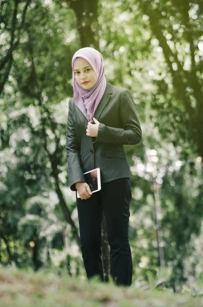 Öğrenci ve iş kavramı, ayakta ve tablet tutan kentsel park arka plan üzerinde takım elbiseli Genç profesyonel hijab kadınlar.