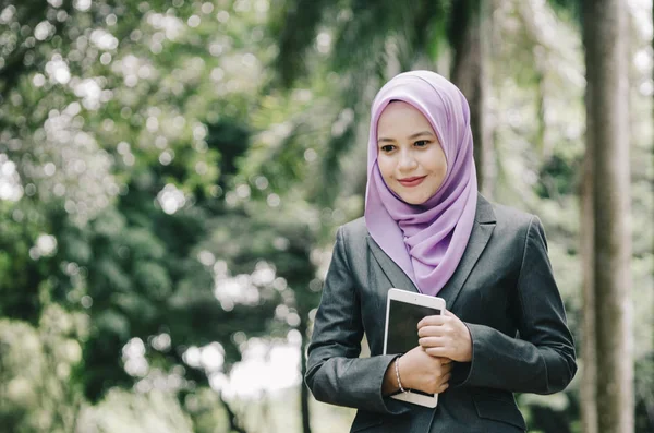 Öğrenci ve iş kavramı, ayakta ve tablet tutan kentsel park arka plan üzerinde takım elbiseli Genç profesyonel hijab kadınlar.