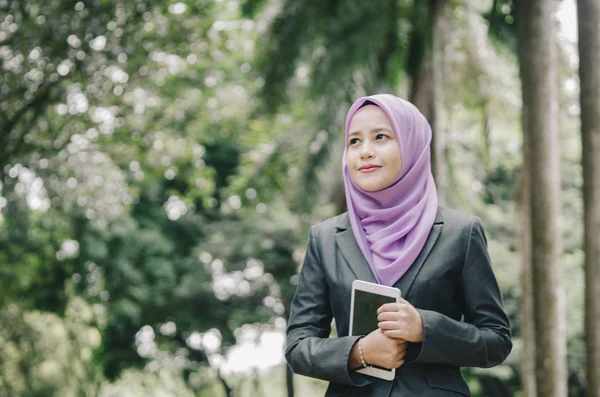 Öğrenci ve iş kavramı, ayakta ve tablet tutan kentsel park arka plan üzerinde takım elbiseli Genç profesyonel hijab kadınlar.