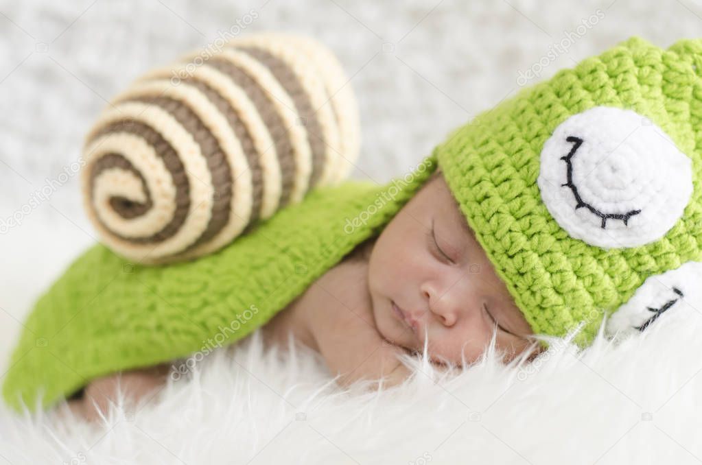 Portrait of sweet newborn baby in knitted snail costume sleeping on white blanket.selective focus shot