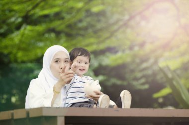 Tasarruf ve eğitim kavramı, Genç Anne oğlunu para tasarrufu öğretmek. Ağacın altında bankta oturmuş
