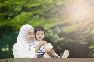Tasarruf ve eğitim kavramı, Genç Anne oğlunu para tasarrufu öğretmek. Ağacın altında bankta oturmuş