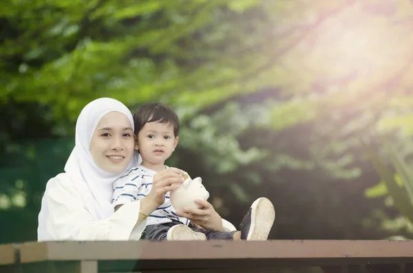 省教育コンセプト若い母親を教える彼女の息子がお金を節約します ツリーの下のベンチに座ってください — ストック写真