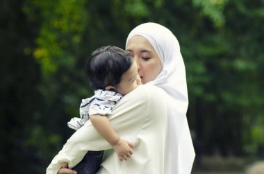 Genç Anne oğlunu mutlu aile kavramı için parlak güneşli bir günde altında Park'ta sarılma