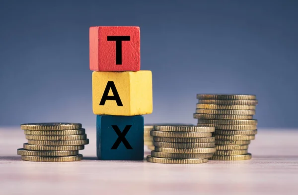 Cubo de madeira com palavra TAX e empilhamento de moeda na mesa de madeira — Fotografia de Stock