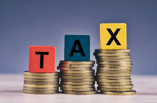 Cubo de madeira com palavra TAX e empilhamento de moeda na mesa de madeira — Fotografia de Stock