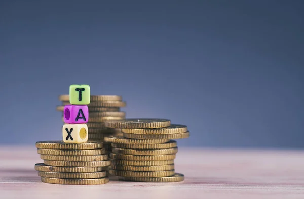 Cubo colorido com palavra TAX e empilhamento de moeda na mesa de madeira — Fotografia de Stock