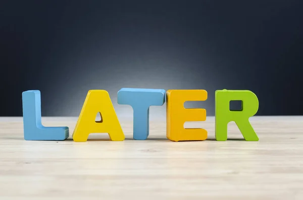 Alphabet word LATER on wooden desk over dark background — Stock Photo, Image