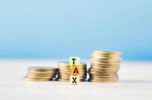 Cubo colorido com palavra TAX e empilhamento de moeda na mesa de madeira — Fotografia de Stock