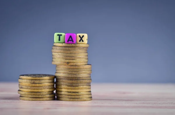 Cubo de madeira com palavra TAX e empilhamento de moeda na mesa de madeira — Fotografia de Stock