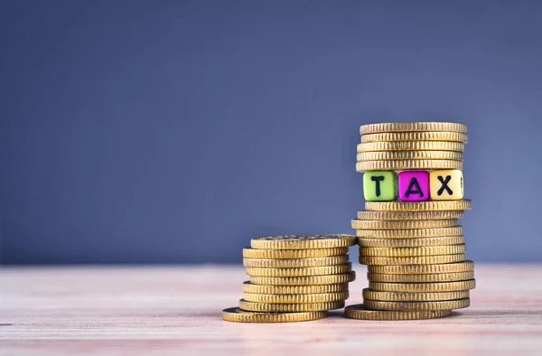 Cubo colorido com palavra TAX e empilhamento de moeda na mesa de madeira — Fotografia de Stock