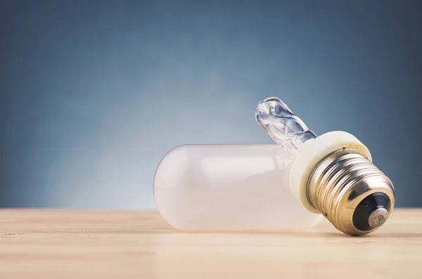 Ampoule cassée sur un bureau en bois sur un fond sombre doucement éclairé — Photo