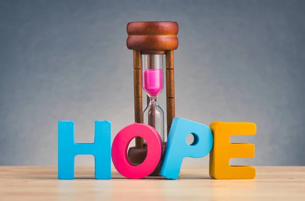 Hourglass and HOPE word made from wooden letter on desk over gently lit dark background — Stock Photo, Image