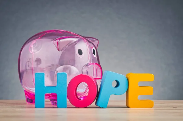 HOPE word made from wooden letter and piggy bank on desk over gently lit dark background — Stock Photo, Image