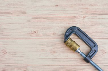 Ahşap arka plan üzerinde bir G-Clamp sıkıca sıkıştırılmış sikkeler