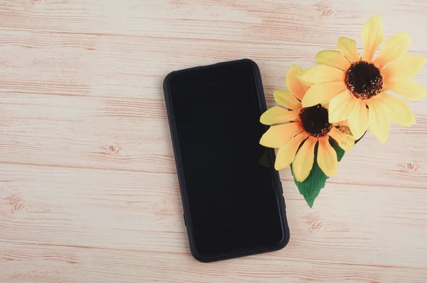 smartphone and artificial plant on wooden desk background