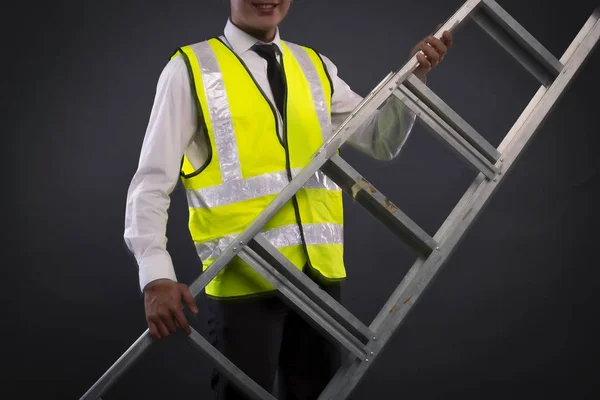 Joven técnico o ingeniero sosteniendo escalera de aluminio sobre fondo oscuro — Foto de Stock