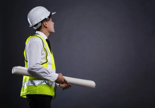 Aufnahme von hinten eines jungen Architekten oder Ingenieurs mit Zeichenpapier vor dunklem Hintergrund — Stockfoto