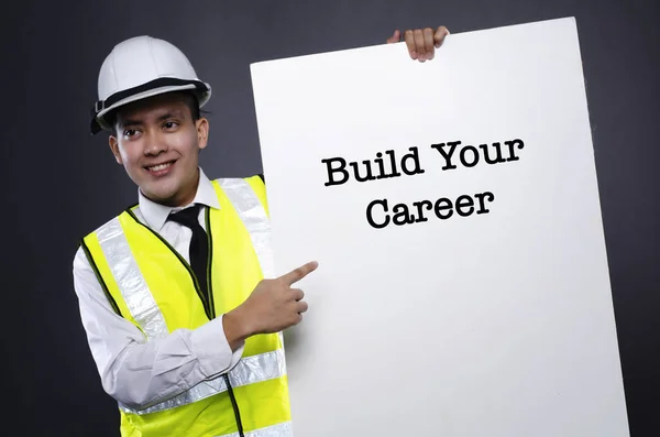 Joven ingeniero o gerente con casco de seguridad blanco apuntando a la tarjeta con la palabra CONSTRUIR SU CARRERA — Foto de Stock