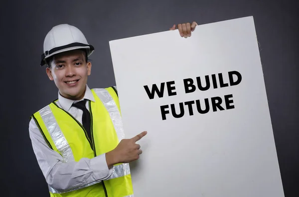 Joven ingeniero o gerente con casco de seguridad blanco apuntando a la tarjeta con la palabra CONSTRUYEMOS FUTURO — Foto de Stock