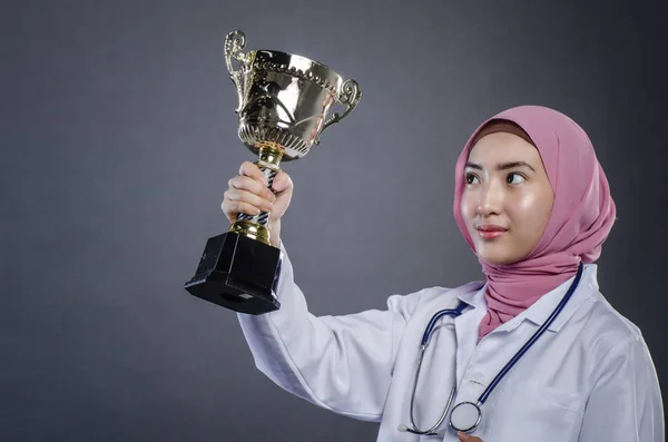 Primer plano retrato de confianza joven hijab médico femenino sosteniendo trofeo sobre fondo oscuro — Foto de Stock