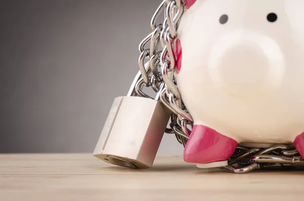 piggy bank surrounded by chains  and padlock on wooden desk