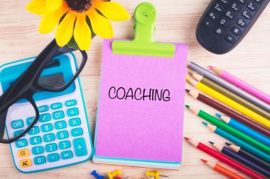 Hesap makinesi, kalem, raptiye ve not defterine yazılmış koçluk kelimeleriyle çalışma masası