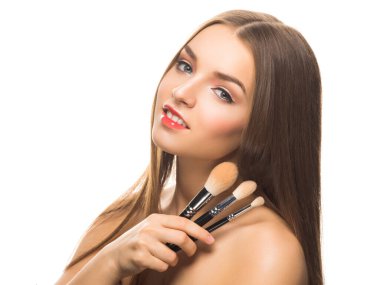 Sofistike makyajlı genç bir bayan model kameraya bakıyor ve beyaz üzerinde izole edilmiş makyaj fırçaları tutuyor..