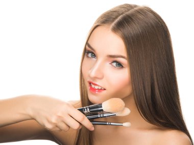 Sofistike makyajlı genç bir bayan model kameraya bakıyor ve beyaz üzerinde izole edilmiş makyaj fırçaları tutuyor..