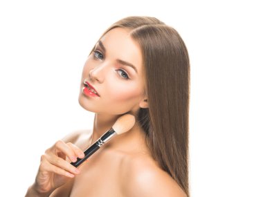 Makyajlı genç bir kadın model kameraya bakıyor ve yüzüne dokunuyor..