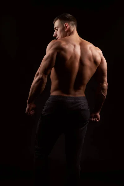 Back view of muscular man against of black background. Studio shot