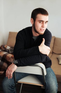 Siyah ceket ve kot pantolon giyen yakışıklı adam içeride oturuyor.