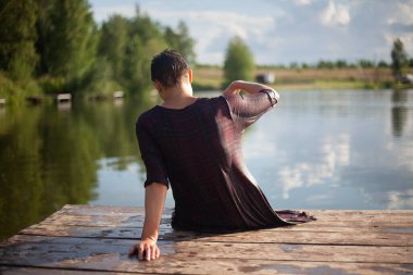 Islak elbiseli bir kız gölün kenarında oturuyor..