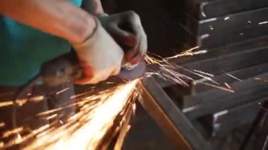 Metal işleme. Öğütücü malzemesi. Sıcaktan kıvılcımlar uçuşuyor. Yapısal bir parça oluştururken atölyede çalış. Yüksek sürtünmeden çıkan parlak metal parçacıkları. Alet ellerde.