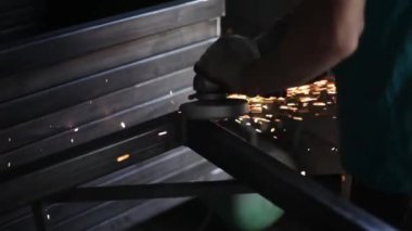 Metal işleme. Öğütücü malzemesi. Sıcaktan kıvılcımlar uçuşuyor. Yapısal bir parça oluştururken atölyede çalış. Yüksek sürtünmeden çıkan parlak metal parçacıkları. Alet ellerde.