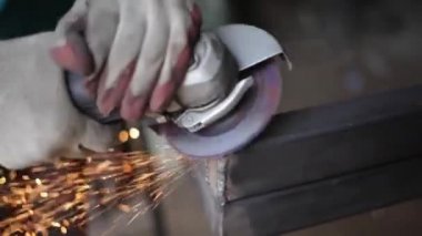 Metal işleme. Öğütücü malzemesi. Sıcaktan kıvılcımlar uçuşuyor. Yapısal bir parça oluştururken atölyede çalış. Yüksek sürtünmeden çıkan parlak metal parçacıkları. Alet ellerde.