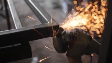 Metal işleme. Öğütücü malzemesi. Sıcaktan kıvılcımlar uçuşuyor. Yapısal bir parça oluştururken atölyede çalış. Yüksek sürtünmeden çıkan parlak metal parçacıkları. Alet ellerde.