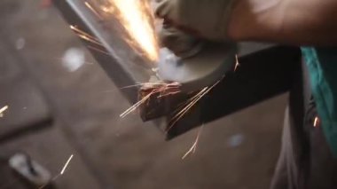 Metal işleme. Öğütücü malzemesi. Sıcaktan kıvılcımlar uçuşuyor. Yapısal bir parça oluştururken atölyede çalış. Yüksek sürtünmeden çıkan parlak metal parçacıkları. Alet ellerde.