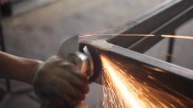 Metal işleme. Öğütücü malzemesi. Sıcaktan kıvılcımlar uçuşuyor. Yapısal bir parça oluştururken atölyede çalış. Yüksek sürtünmeden çıkan parlak metal parçacıkları. Alet ellerde.