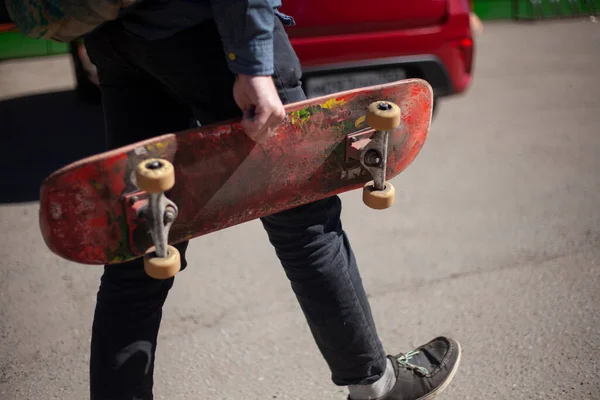 Skateboard in der Hand des Kerls. Der Mann trägt das Brett in der Hand. — Stockfoto