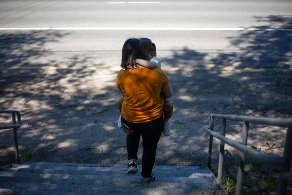La niña lleva al niño por los escalones. Joven madre en la calle con una chica en sus brazos. — Foto de Stock