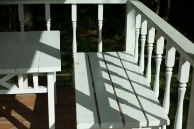 Yazlık verandada beyaz masa ve bank. Tahta mobilyalar. 19. yüzyılın stilisti.