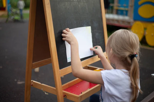 The child draws at the easel on the street.