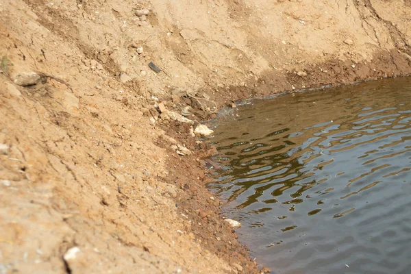 Stranden på en konstgjord damm. En hög med sand på vattnet. — Stockfoto