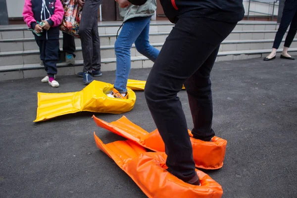 As crianças colocam as pernas dos patos. Sapatos engraçados para jogar catch-up. Festa infantil na rua. — Fotografia de Stock