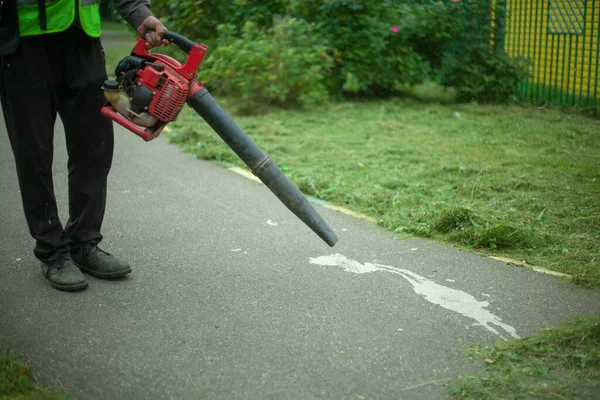 Tukang kebun menggunakan blower untuk menghapus rumput kering dari jalan. — Stok Foto