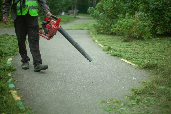 Tukang kebun menggunakan blower untuk menghapus rumput kering dari jalan. — Stok Foto