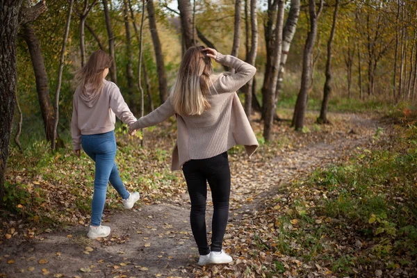 A lányok fogják egymás kezét és átsétálnak az erdőn. Barátnők egy séta a parkban ősszel. — Stock Fotó