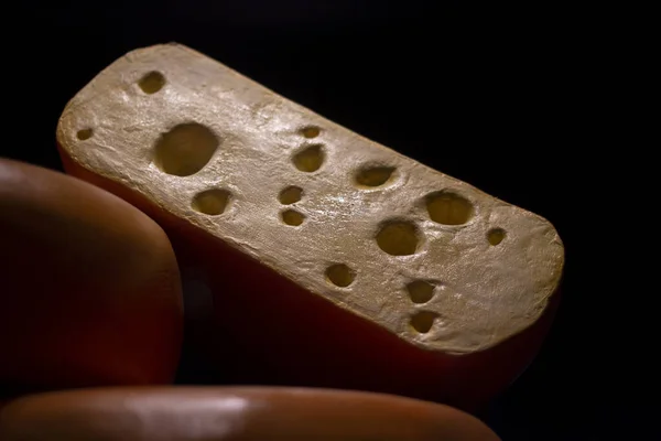 A piece of cheese in low light. Cheese with holes. Natural product. Food on the counter.